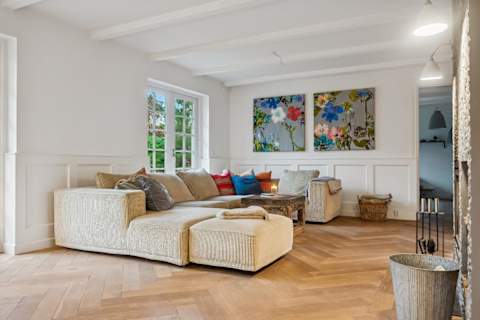 A bright and inviting living room with generous seating, soft textures and natural light — designed for relaxed afternoons, quiet evenings and shared moments together.