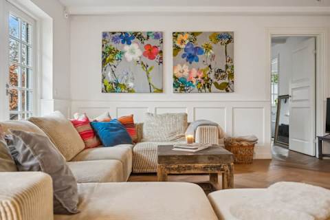 A bright and inviting living room with generous seating, soft textures and natural light — designed for relaxed afternoons, quiet evenings and shared moments together.