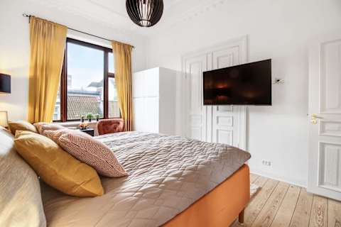 Elegant and spacious bedroom with a luxurious king-size bed, refined décor, generous storage, and a large flat-screen TV. A calm, high-end retreat designed for comfort and relaxation in central Aarhus.