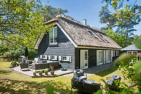 A beautifully thatched summer house surrounded by greenery, offering a warm, inviting atmosphere and a peaceful setting designed for slow days and shared moments. Just Steps From Hornbaek Beach