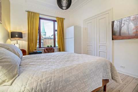 Elegant and spacious bedroom with a luxurious king-size bed, refined décor, generous storage, and a large flat-screen TV. A calm, high-end retreat designed for comfort and relaxation in central Aarhus.