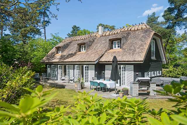 A beautifully thatched summer house surrounded by greenery, offering a warm, inviting atmosphere and a peaceful setting designed for slow days and shared moments. Just Steps From Hornbaek Beach