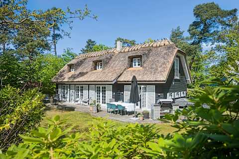 A beautifully thatched summer house surrounded by greenery, offering a warm, inviting atmosphere and a peaceful setting designed for slow days and shared moments. Just Steps From Hornbaek Beach